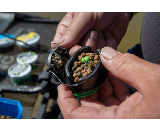 marinwe 2 - freddiethepillowandfriends.co.uk Close-up of hands assembling a fishing lure with brown bait pellets and a bright green bead inside the hook housing.